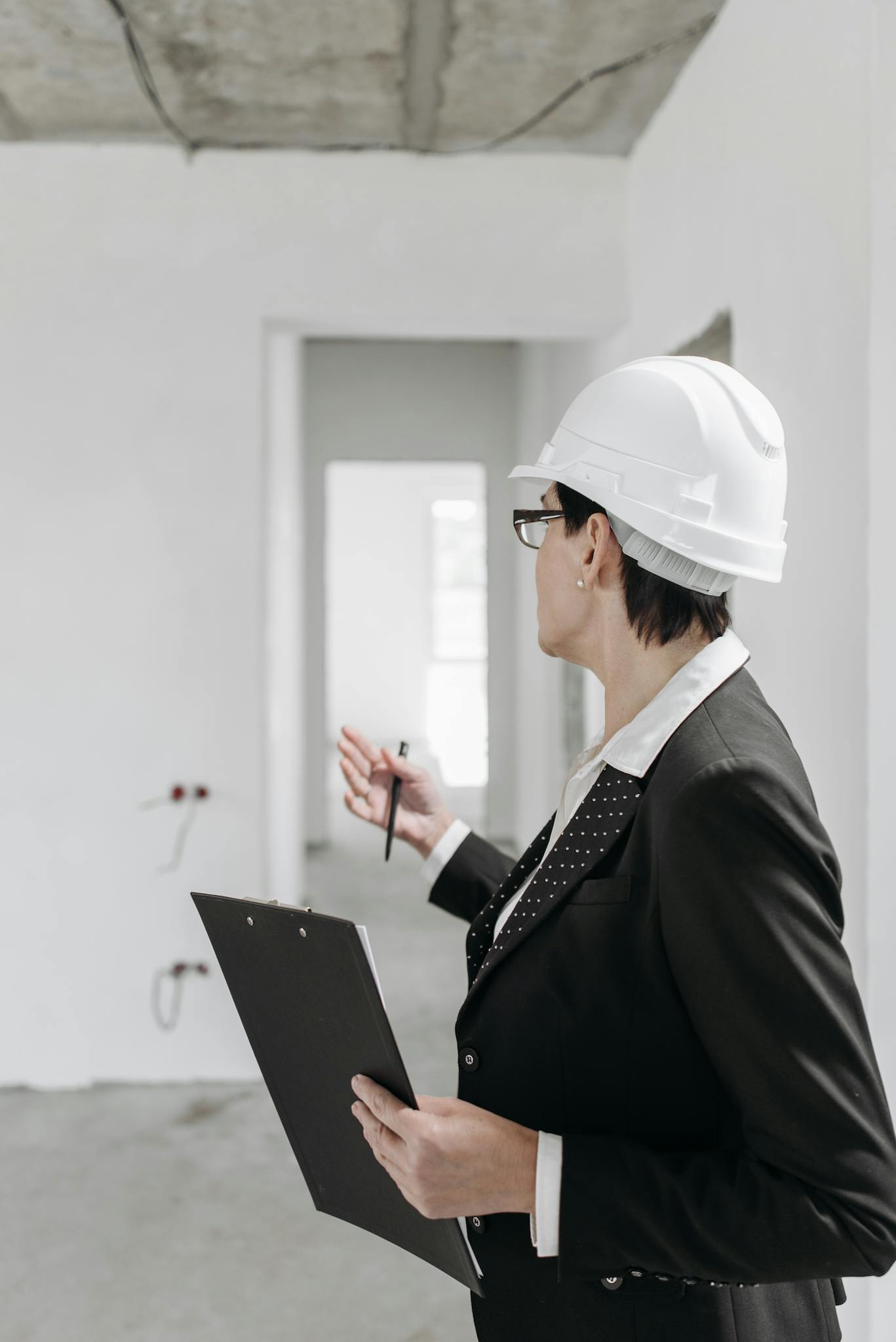 A professional engineer in a suit and hard hat inspecting a construction site with a clipboard.