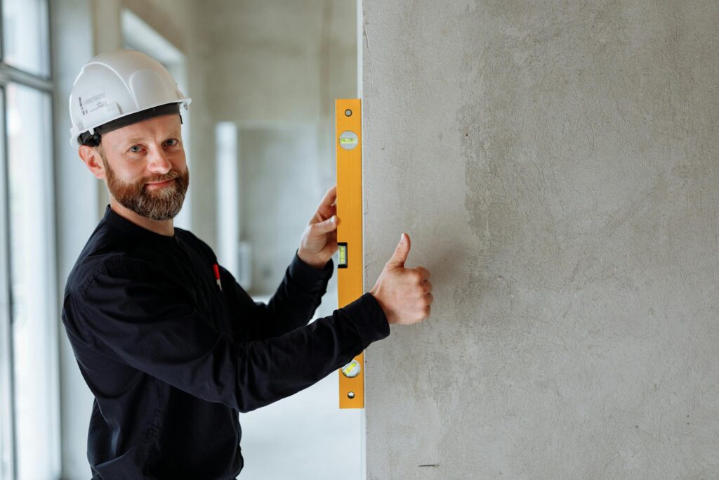 Confident male construction worker using a spirit level on a concrete wall for precise alignment indoors.